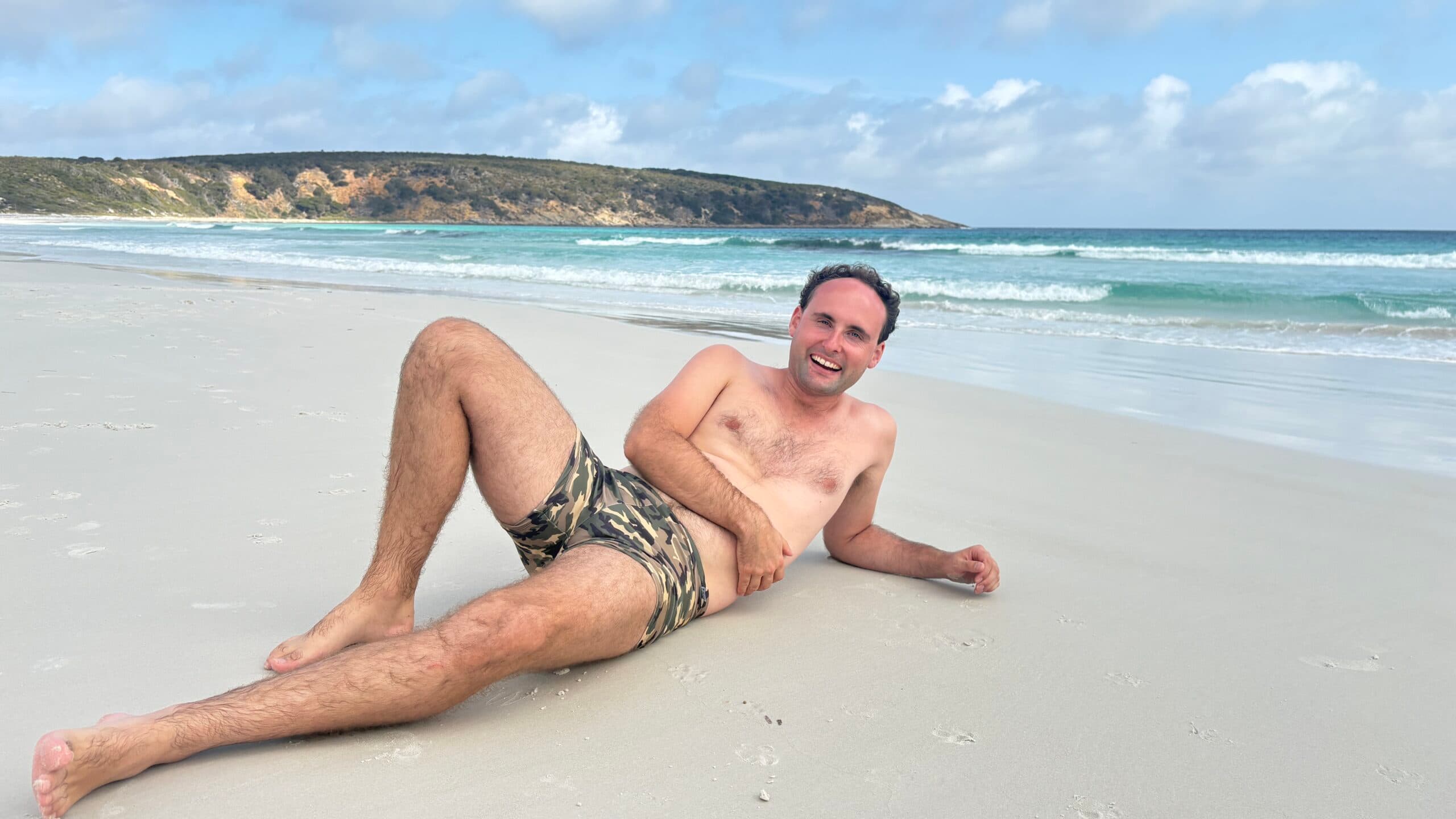 Model in patterned swim briefs reclining on the sand